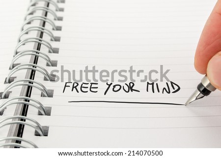 Close-Up of Hand with Pen Writing in Black Ink Free Your Mind in Spiral Bound Notebook.