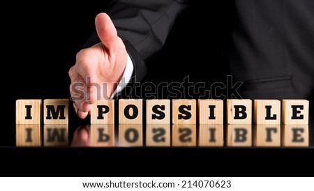 The word Im - Possible on a line wooden blocks separated by the hand of a businessman conceptual of all things being possible given enough input and effort, on a dark background with copyspace.