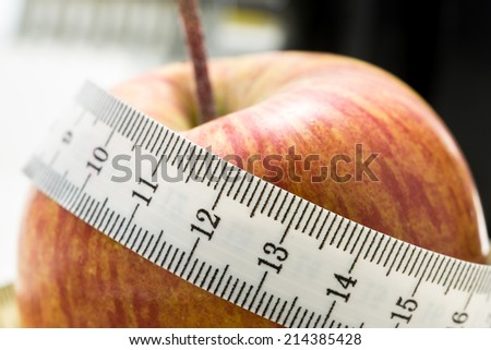Fresh juicy red apple wrapped in a tape measure with a close up shallow dof view of the centimeter scale on the tape conceptual of a healthy diet and weight loss.