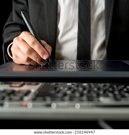 Businessman using a tablet and stylus to navigate on his desktop computer , close up low angle view of his hand across the computer keyboard.