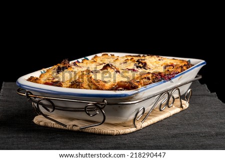 Delicious homemade plum pie with a golden pastry crust standing ready to serve on a metal stand in an oven dish, dark background.