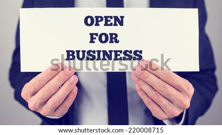 Close up of the hands of a businessman holding a white sign or card with the message - Open For Business.