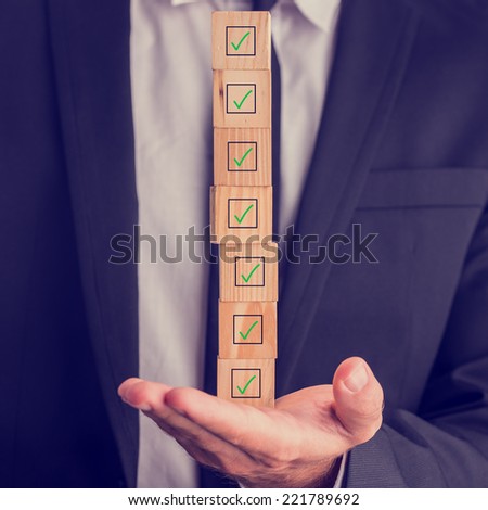 Businessman holding a stack of checked boxes marked on wooden cubes balanced on his hand conceptual of quality, completion, approval or voting.
