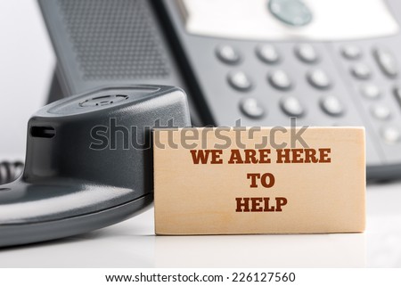 Simple Customer Support Concept Design- Close up of Small Wooden Piece with We are Here to Help Texts at the Customer Service Operator Desk with Telephone.