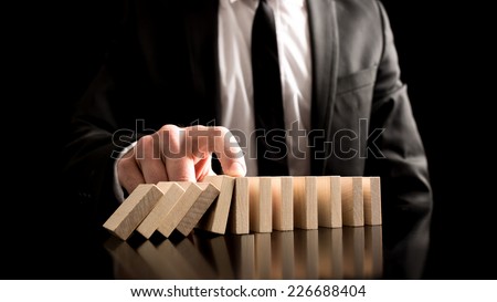Businessman Stopping the Domino Effect from Small Wooden Blocks on the Table. A Creative Concept for Solution to Problem.