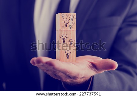 Businessman holding three wooden cubes vertically aligned, with hand-drawn incandescent light bulbs, concept of creative ideas and new business projects.