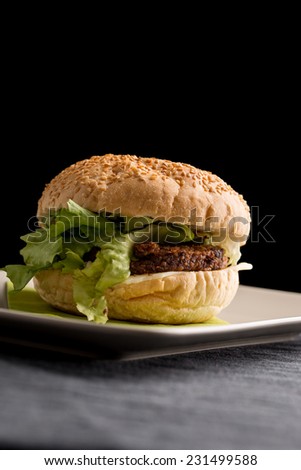 Close up Tasty Burger with Vegetarian Rissoles and Fresh Lettuce on White Plate, Dine on a Table. Isolated on Black Background.