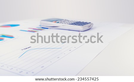 Desk calculator next to printed business documents with different diagrams as line, pie or columns charts, concept of financial analysis and data representation.
