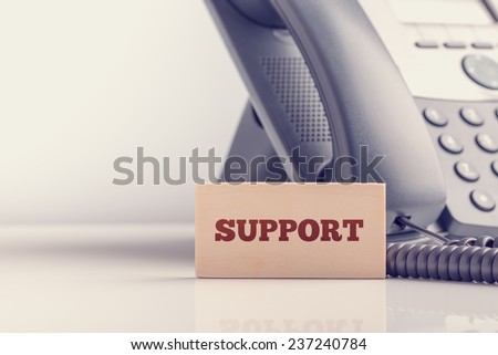 Retro image of business telephone support concept with a small wooden sign saying - Support - standing alongside a landline telephone instrument with copyspace.
