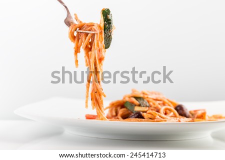 Spaghetti with tomato sauce and courgette on a fork over white plate.