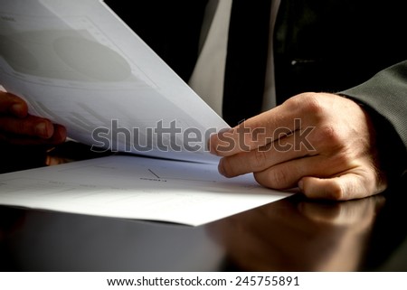 Close up of the hands of a business man analyzing business papers and holding a spreadsheet with statistics in his hand.