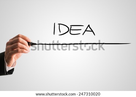 Man writing the word Idea with a black marker pen from behind a virtual screen or interface on a light grey background with copyspace, close up view of the text and his hand.