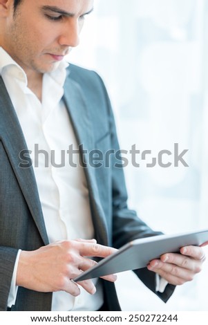Businessman standing using a tablet computer over a high key background. Focus to the tablet.