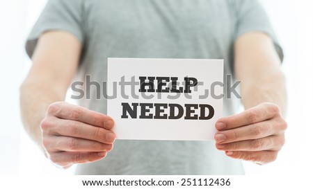 Man in a grey t-shirt holding a white card with Help needed sign representing a job offer or problematic of homeless people.