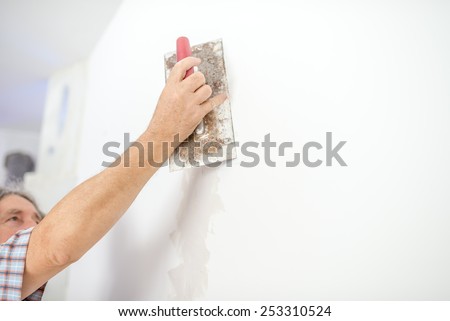 Man plastering a white wall preparing it for painting or wallpapering in a DIY and home decoration or renovation concept.