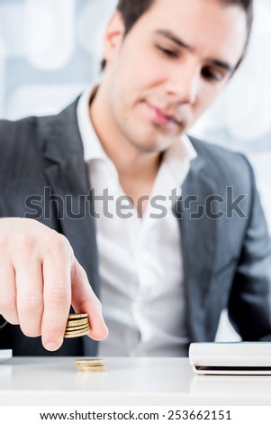 Businessman sitting at his white desk counting gold Euro coins in a conceptual image, focus to his hand.