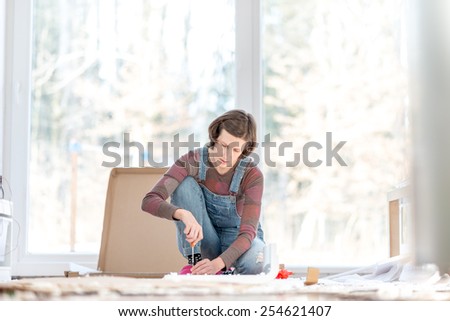 Young woman doing DIY repairs at home putting together self assembly furniture using a screwdriver.