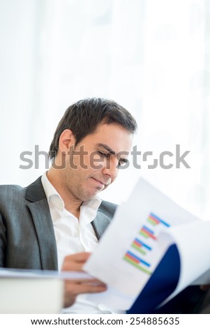 Businessman reading an analytical report studying the graphs and statistics as he sits at his desk, focus to his face.