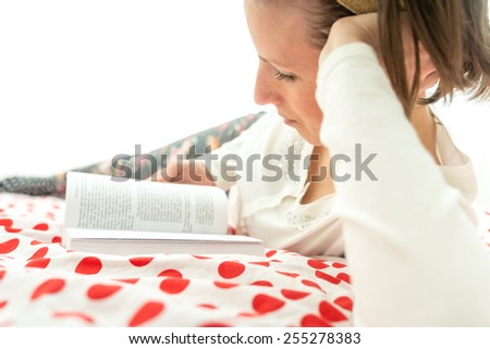 Young woman relaxing on her bed with a book lying propped up on her elbow ready the story on a red and white polka dot bedspread.
