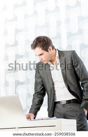 Young male executive standing by his desk making a last glimpse at some document on his laptop computer as he heads off to a meeting or other obligation.