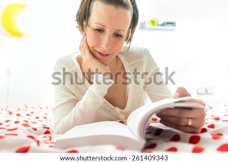 Young brunette reading an interesting novel or studying comfortably lying on her red and white polka dot bedspread.