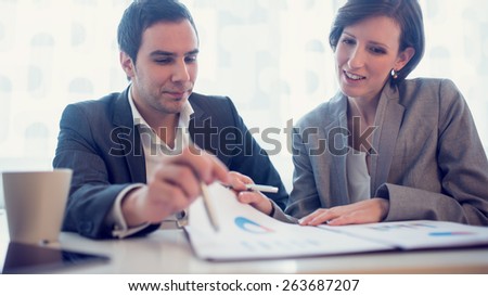 Young female and male business executives looking at business papers or report and cheerfully discussing their success, with a faded retro look.