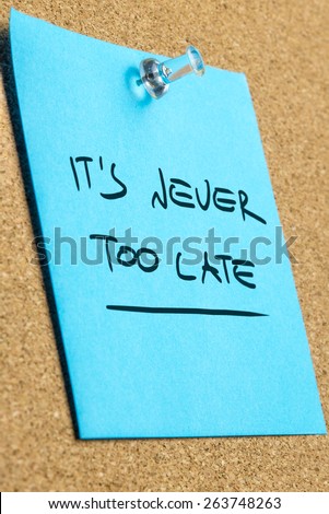 Conceptual Its Never Too Late Phrase on a Light Blue Sticky Note Pinned on the Cork Board, Captured in Close up.