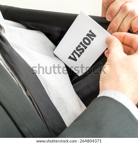 Businessman removing or placing a white card with word Vision in the inner pocket of his suit jacket.