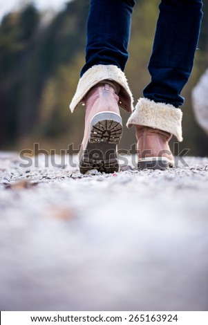 Low angle view with shallow dof of the feet of a woman in jeans and ankle high leather boots walking along a rural path away from the camera. Conceptual of outdoors activity.