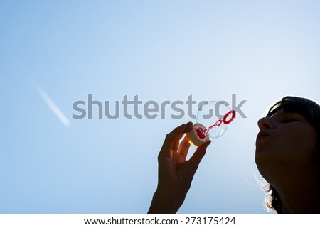 Low angle close up view of the silhouette of a woman blowing bubbles against a sunny blue sky with plenty of copyspace in a conceptual image.