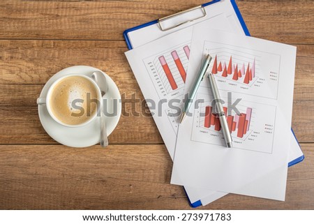Top view of business statistical annual report of profit and income presented in graphs on a rustic wooden office desk with fresh cup of coffee.
