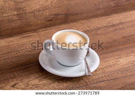 White cup of delicious aromatic freshly prepared cappuccino with generous portion of soft cream on a rustic wooden table.