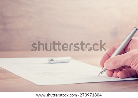 Retro image of businessman hand signing contract or other important documents on a rustic wooden desk.