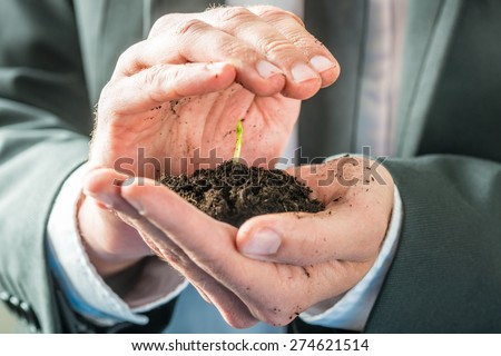 Businessman holding a sprouting seedling in fertile earth cupped in the palm of his hand in a conceptual image of environmental awareness or business startup.