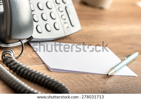 Pen lying on blank white note cards next to a landline telephone on a wooden office desk. Copy space ready for your notes or text.