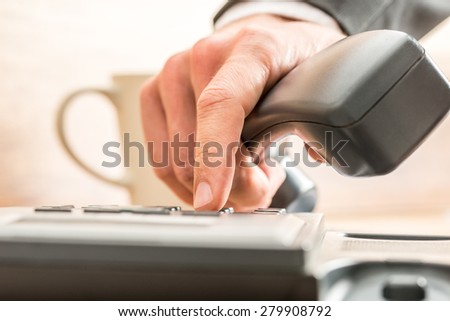 Close up of the fingers of a business adviser dialing out on a land line telephone pressing the number keys on the keypad in a communications concept.