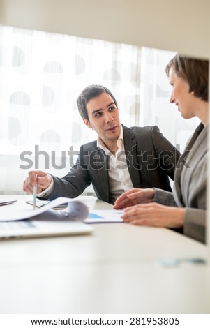 Two Young Business People in Corporate Attire Discussing Some Plans at the Table with Plenty of Documents.