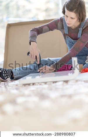 Competent young woman assembling flat pack furniture using a handheld drill as she braces it with her leg for stability.