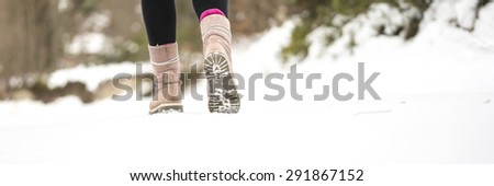 Winter adventures - closeup of warm female winter boots walking on a snowy path outdoors in a cold nature.
