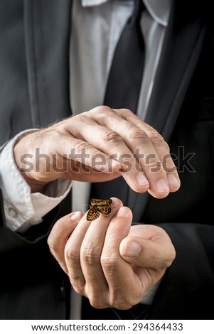 Businessman nurturing a butterfly that has settled on his fingers carefully cupping his hand over the top in a conceptual image.