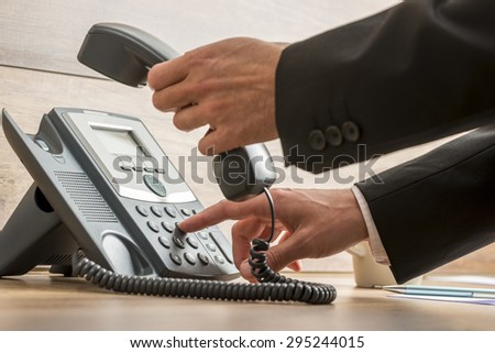Communication operator dialing a telephone number while holding a handset on a classical landline phone about to make a call.