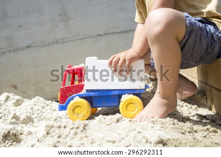 Young Boy Playing with his Plastic Truck Toy on White Sand in his sandbox on a Hot Sunny Summer Day.
