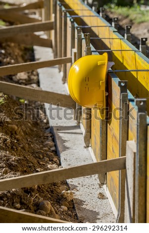 Yellow hardhat hanging outdoors in the sunshine from supported wooden panels on a building site in a construction and building concept.