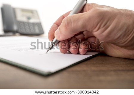 Businessman or lawyer signing important document, legal papers, contract or report on a rustic wooden office desk with a landline telephone in background.