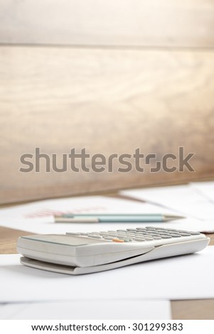 White plastic desk calculator on a printed document, work papers  or assignment, on a wooden desk or workspace, close-up. Suitable for business, accounting, education or science  and research concept.