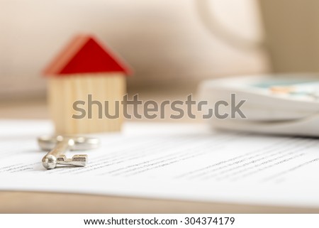 Closeup of contract of house sale ready to be signed with wooden toy house, house key and calculator on it. Conceptual of real estate, mortgage and lease.