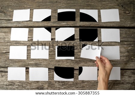 Question or query - solution or answer concept with a woman laying out rows of memo notes with a question mark and placing the last piece in place on the wooden background, close up of her hand.