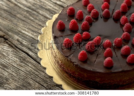 Overhead view of tasty raw chocolate cake decorated with raspberries inviting you to indulge yourself into sweet temptation, placed on a golden plate and textured rustic wooden desk.