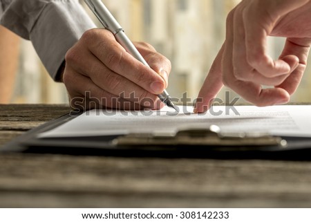Closeup of businessman showing his new business partner where to sign an agreement or contract with fountain pen  on rustic wooden desk.
