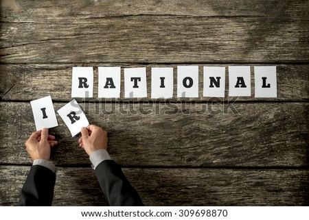 Male hands taking away letters IR from the word Irrational changing it into rational spelled on white cards over rustic textured wooden planks. Conceptual of being objective in decision making.